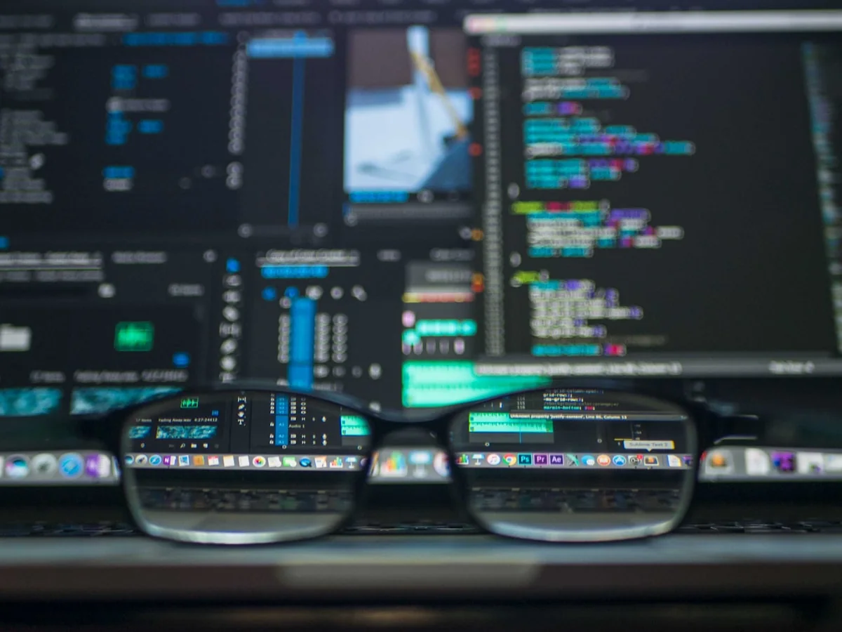 Glasses reflecting code on a computer screen in a programming workspace.