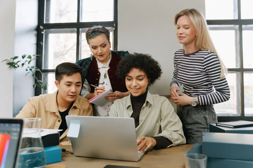 Four colleagues gathered around a laptop at an office table.