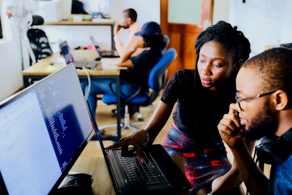 Colleagues reviewing work together at office computers.