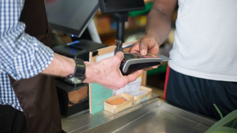 A shopkeeper handing a card payment terminal across the counter to a customer
