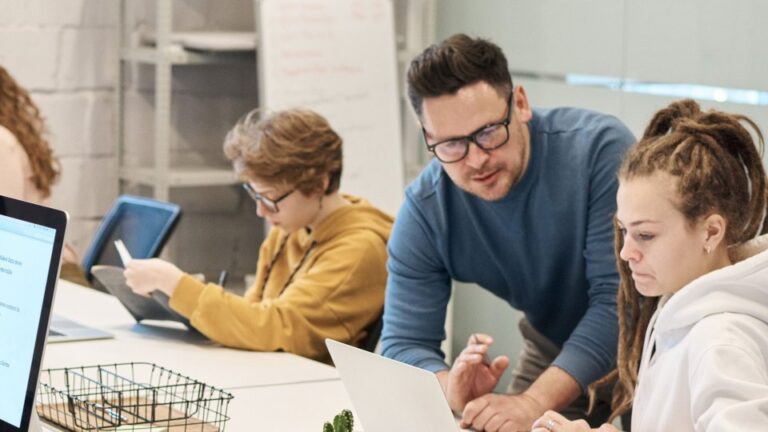 One person leaning in over a colleague's shoulder to look at something on a laptop