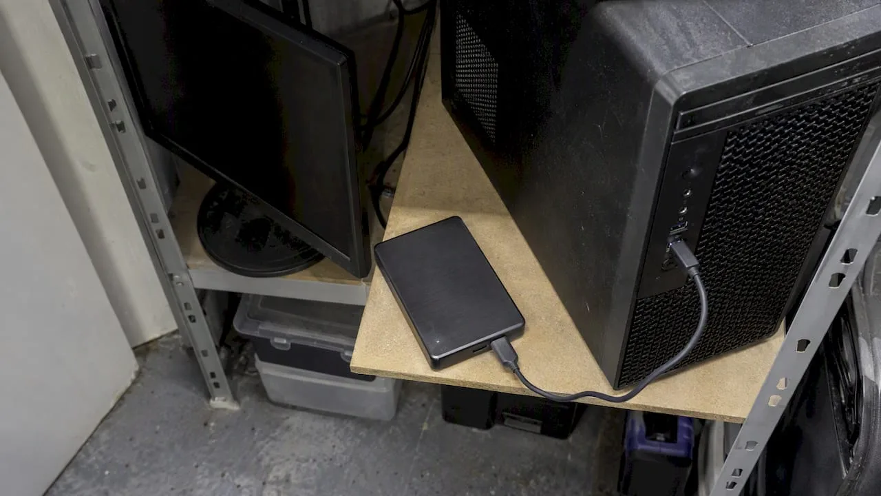 External drive connected to a desktop computer on shelving; illustrative backup equipment.