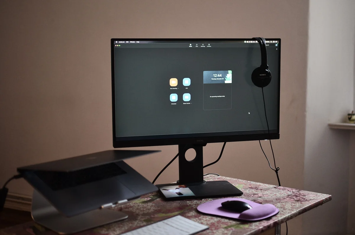A desktop monitor, headset, keyboard and mouse on a desk.